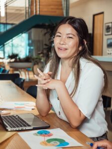 Une femme souriante dans un espace de travail, assise avec un ordinateur portable et des graphiques colorés.