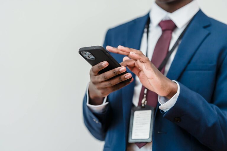 Un professionnel en costume utilisant un smartphone à l'intérieur, concentré sur l'interaction avec l'écran.